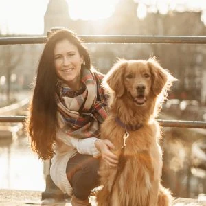 A woman with her dog smiles to the camera in the canals of Amsterdam.