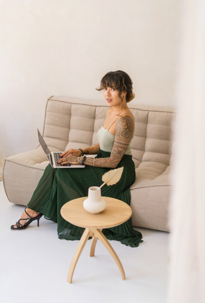 A roman is sitting on a sofa with her laptop for her personal branding photo.