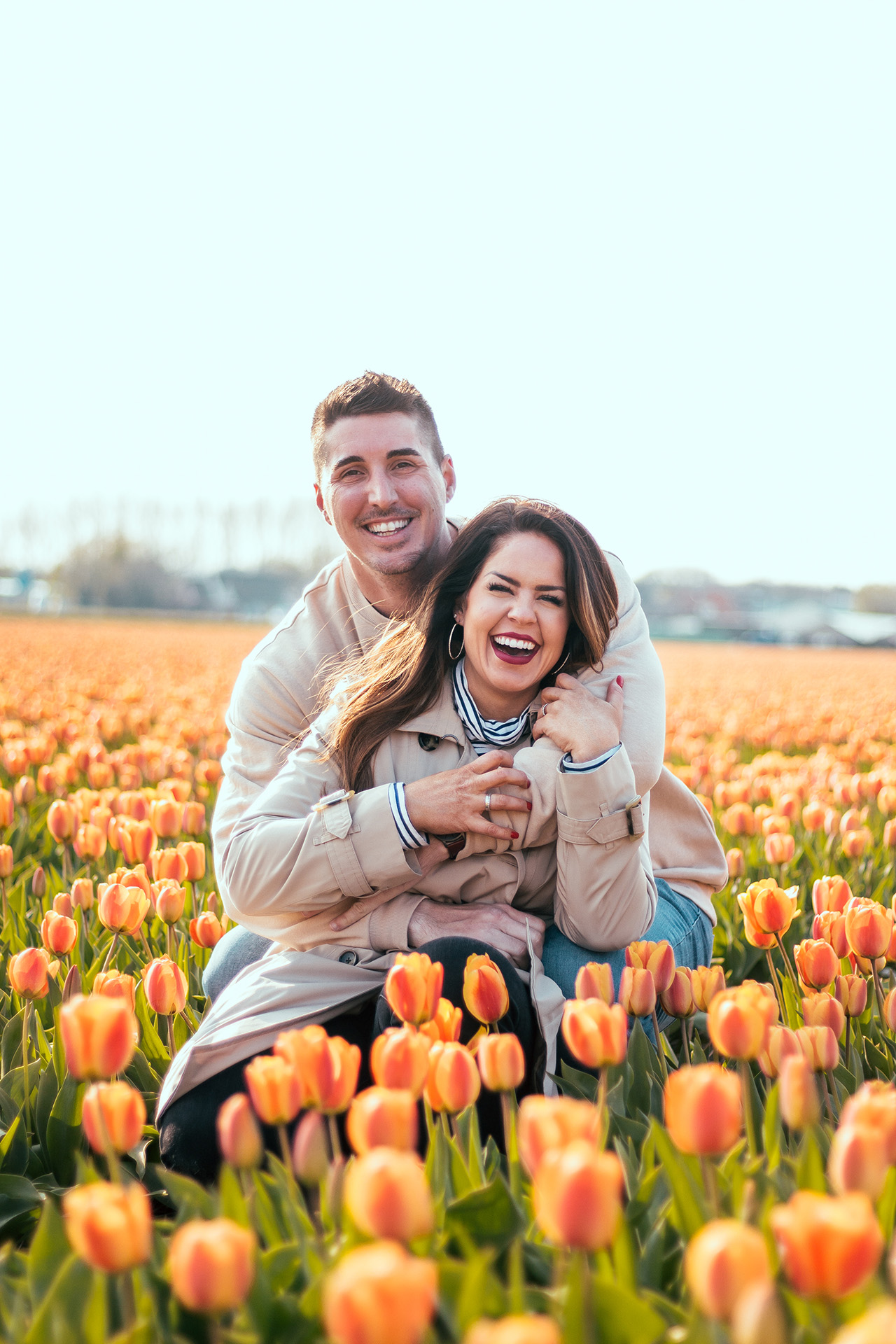 An orange tulip field surrounds a couple hugging each other and laughing at the camera.