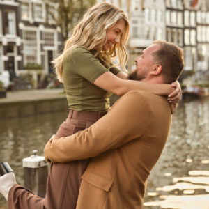 A man is smiling and holding up his newly fiancée in Amsterdam's canals.