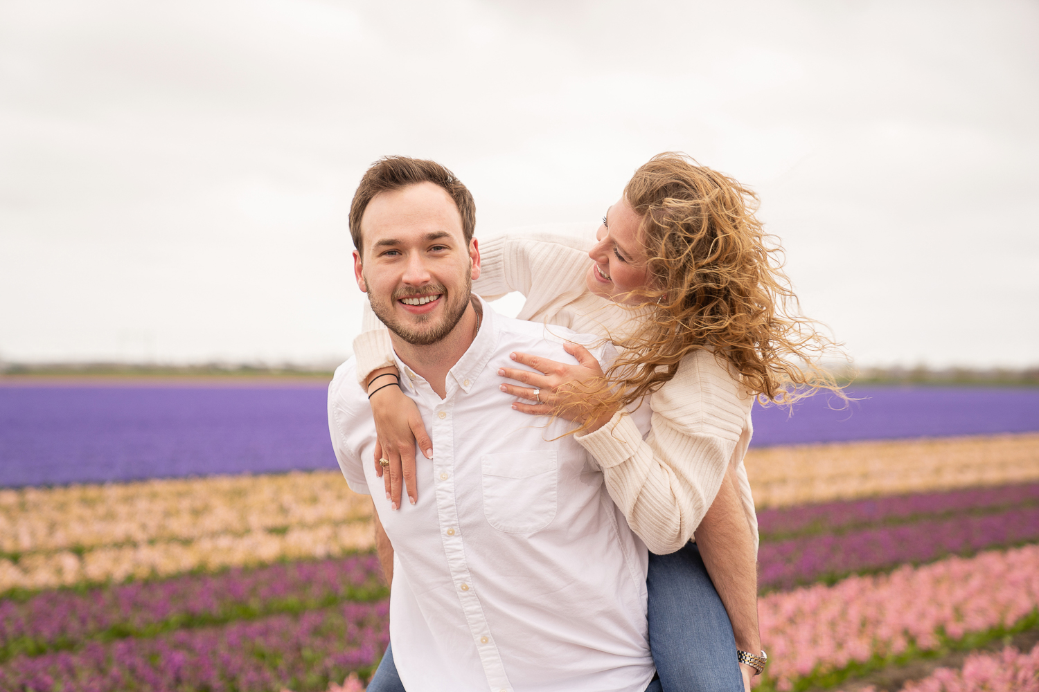 Woman is piggyback on her fiancee surrounded by pink and purple hyacinth fields in Lisse.