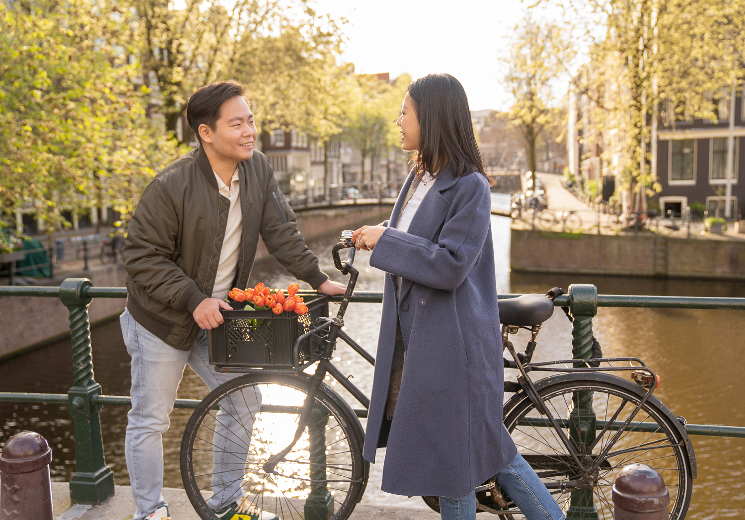 A Chinese couple stare romantically at each other. The woman is holding the bike by the handles and has a bouquet of orange tulips in the bike's basket.