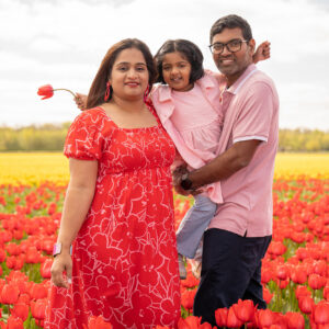 An Indian family of 3 happy surrounded by red tulip fields.