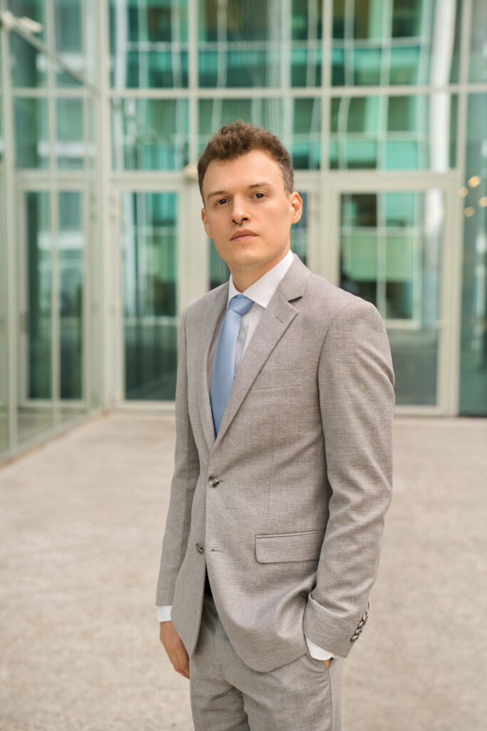A LinkedIn portrait of a man in a grey suit with a corporate background.