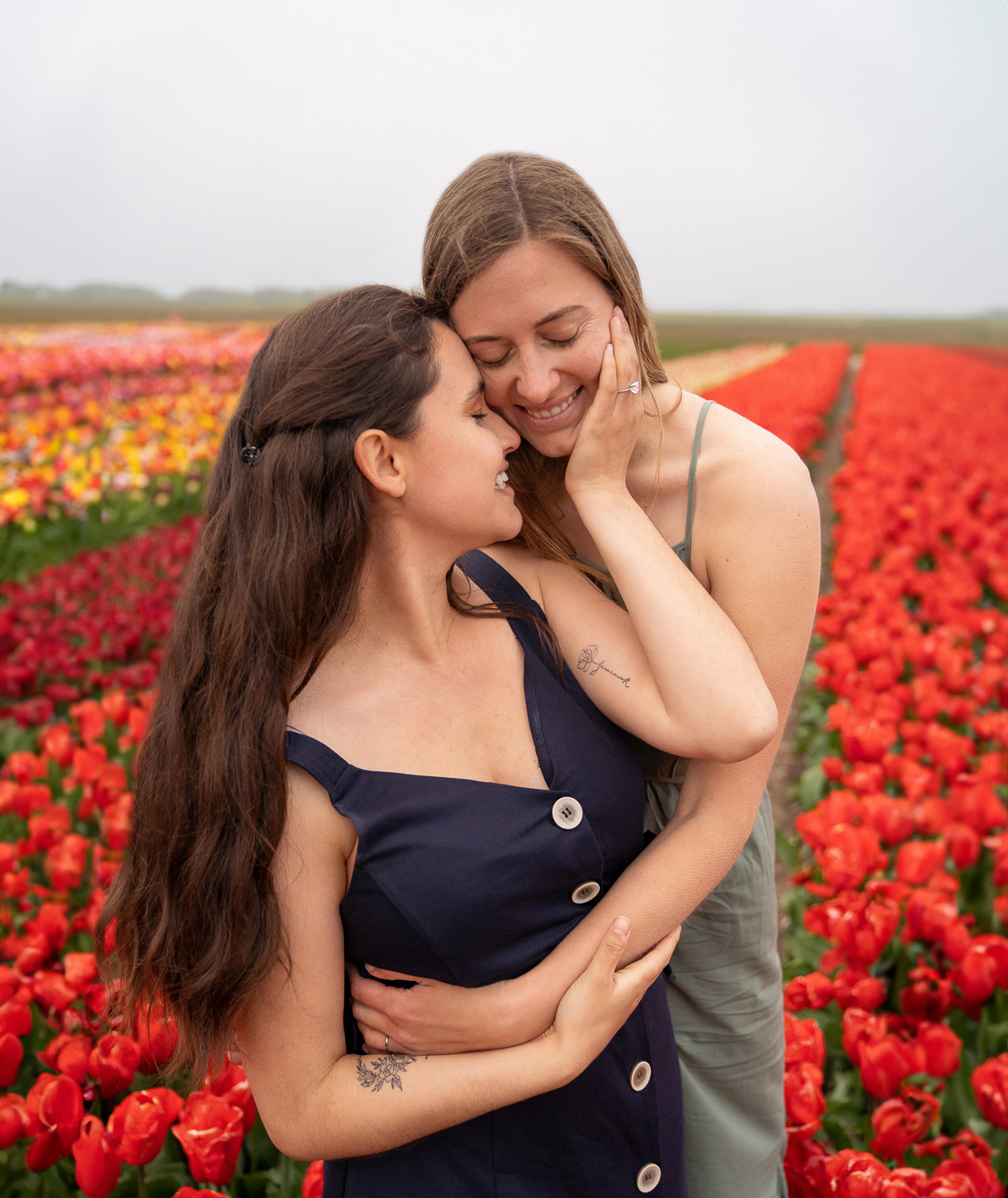 A cute lesbian couple hugging each other between the red tulip fields during their proposal shoot.