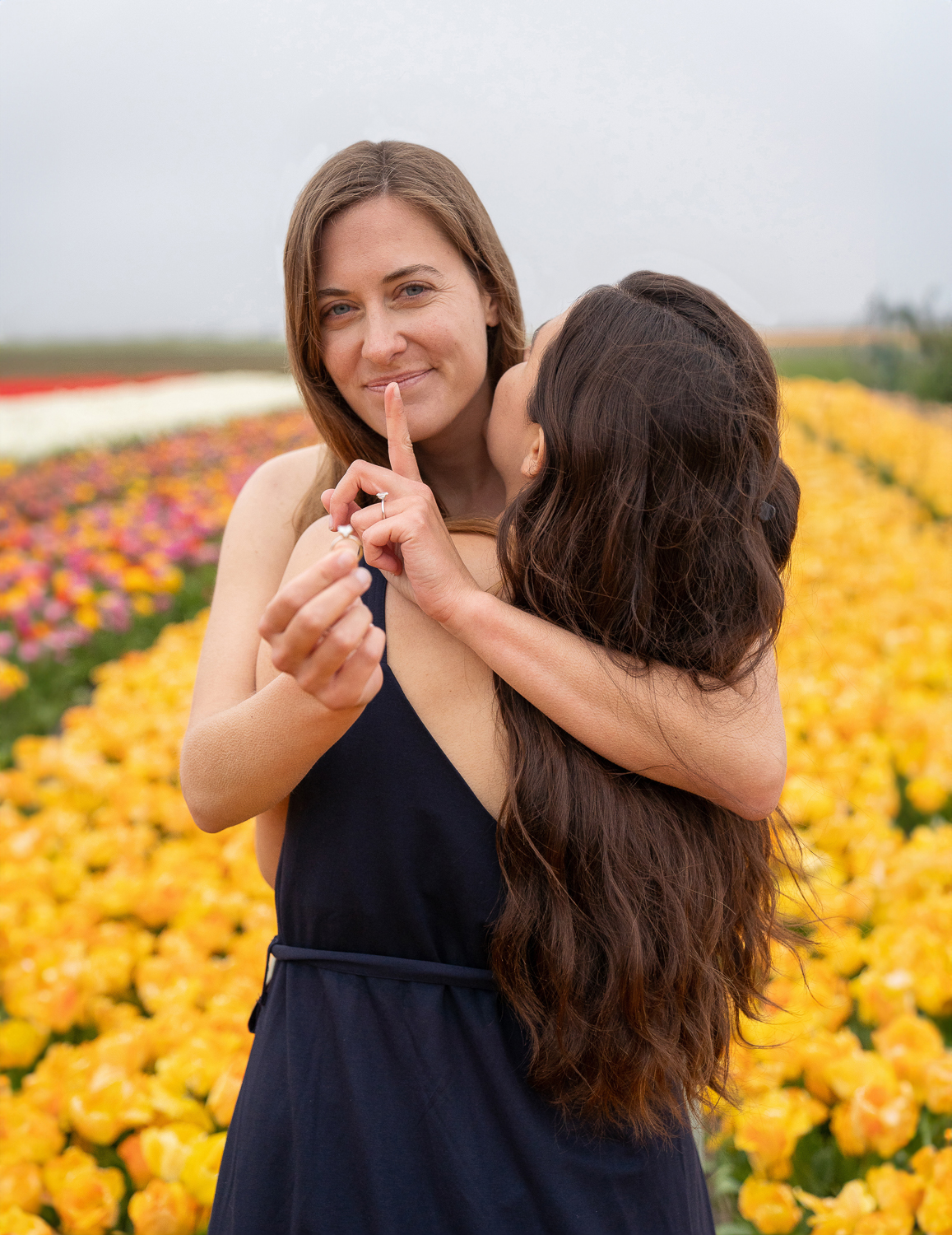 Woman hiding a ring behind for making a surprise proposal to her girlfriend surrounded by orange tulip fields.