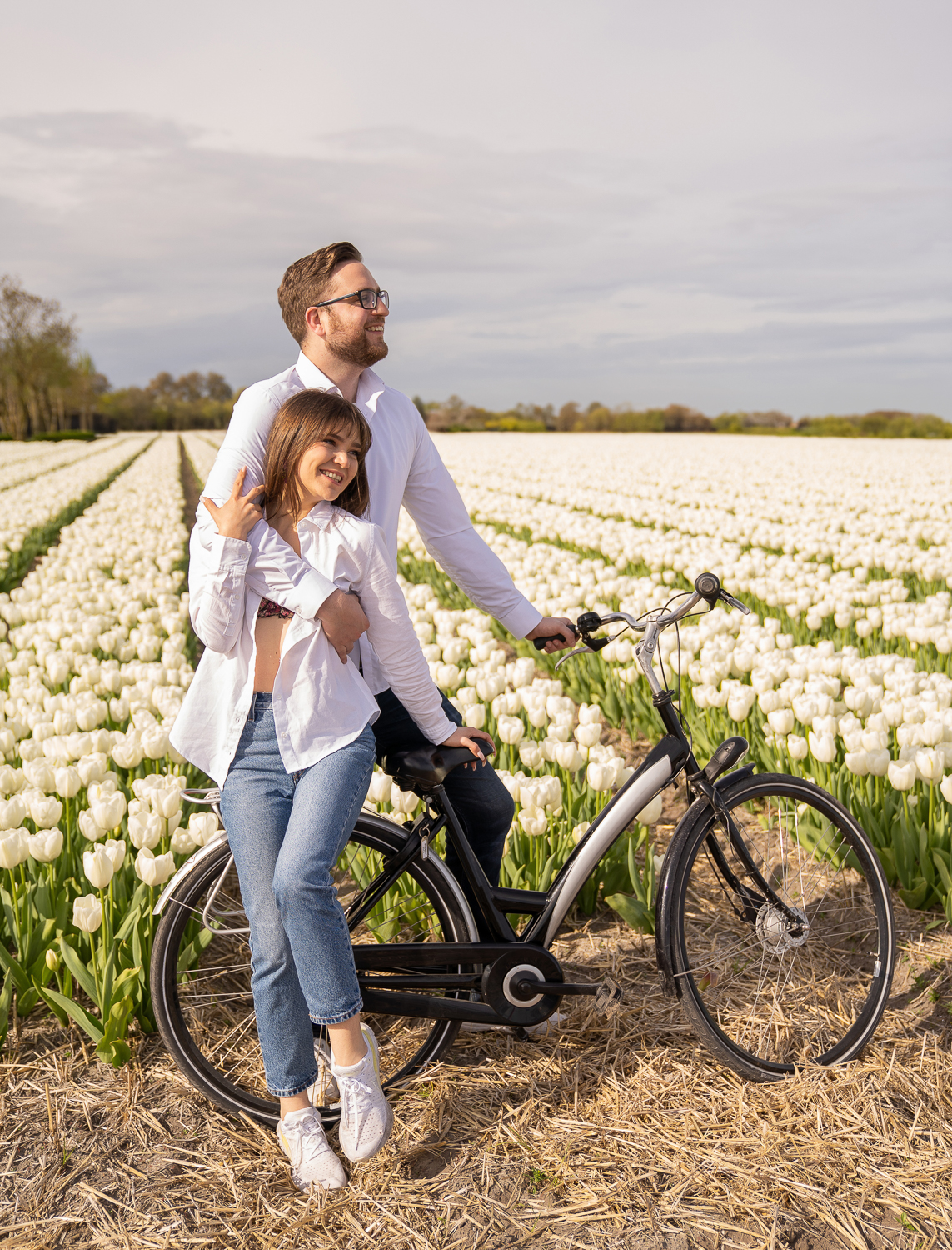 A smiling couple with a bike next to white tulip fields.