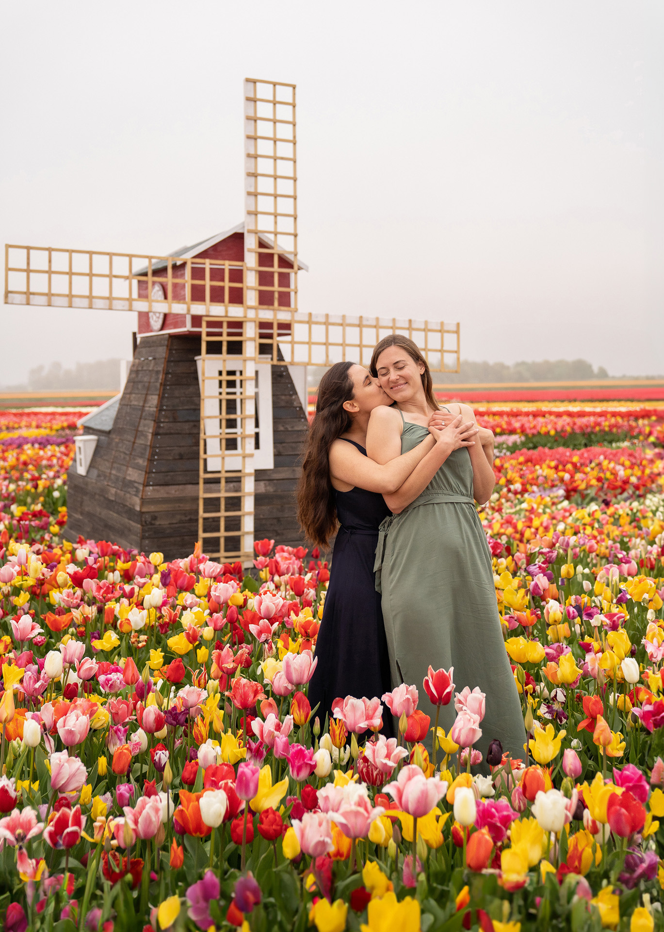 A lesbian couple with a windmill as backdrop in a tulip farm in The Netherlands.