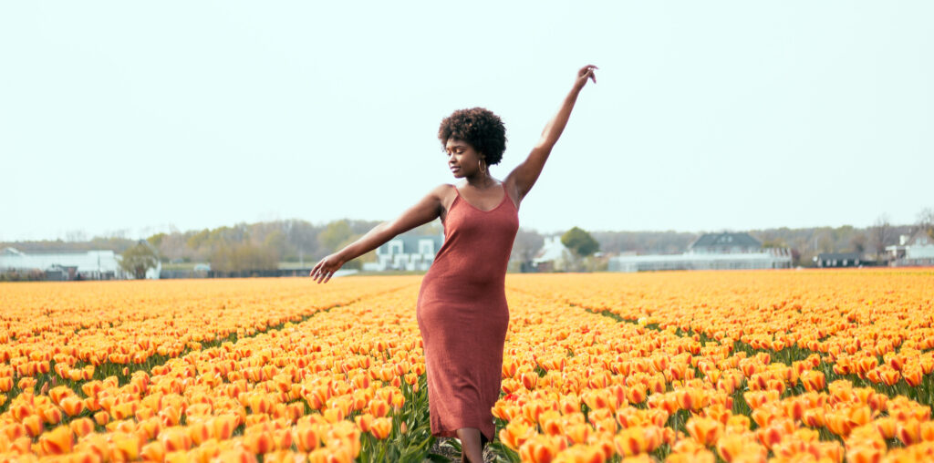 A black woman with afro hair moving her hands surrounded by the beauty of the tulip fields in the Netherlands.