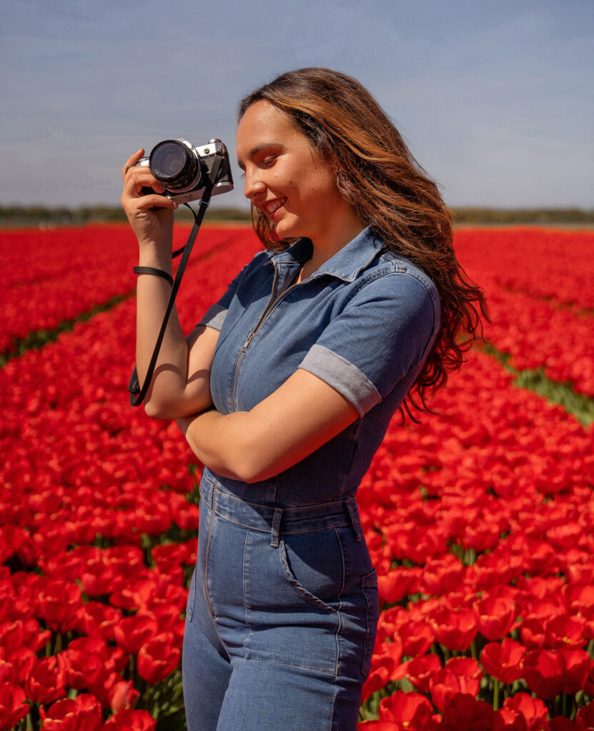 An Amsterdam photographer smiling and holding her camera surrounded by red yellow tulip fields.