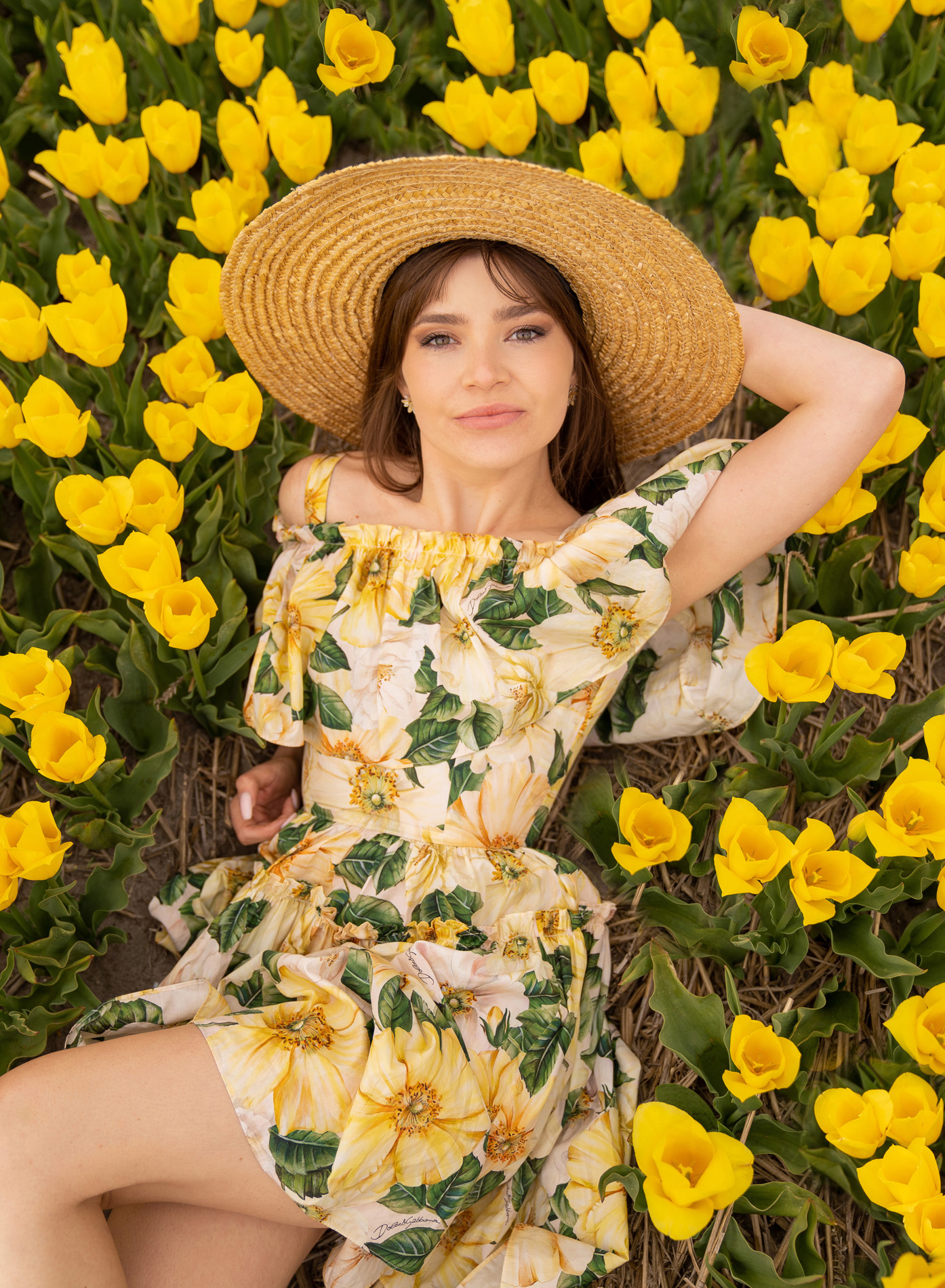 During her tulip photoshoot, a woman lies on the ground surrounded by yellow tulip fields.