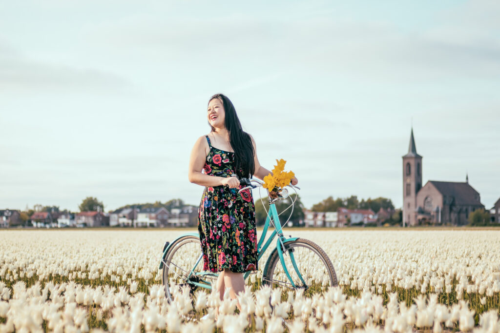 A chinese woman smiling exploring with a bike amongst white tulip fields in the Netherlands.