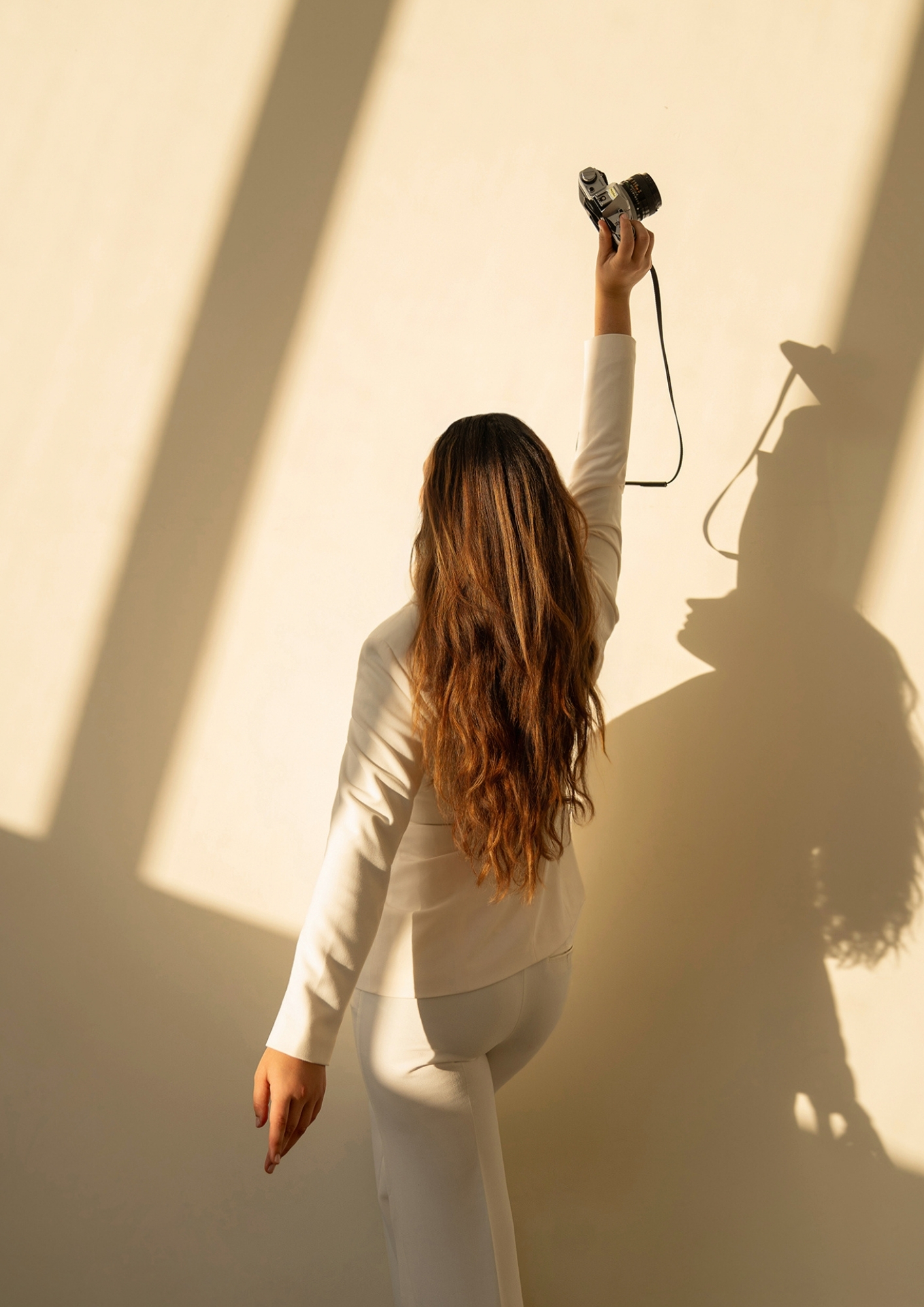 Woman in a cream blazer raising her arm, her shadow cast on a warm sunlit wall