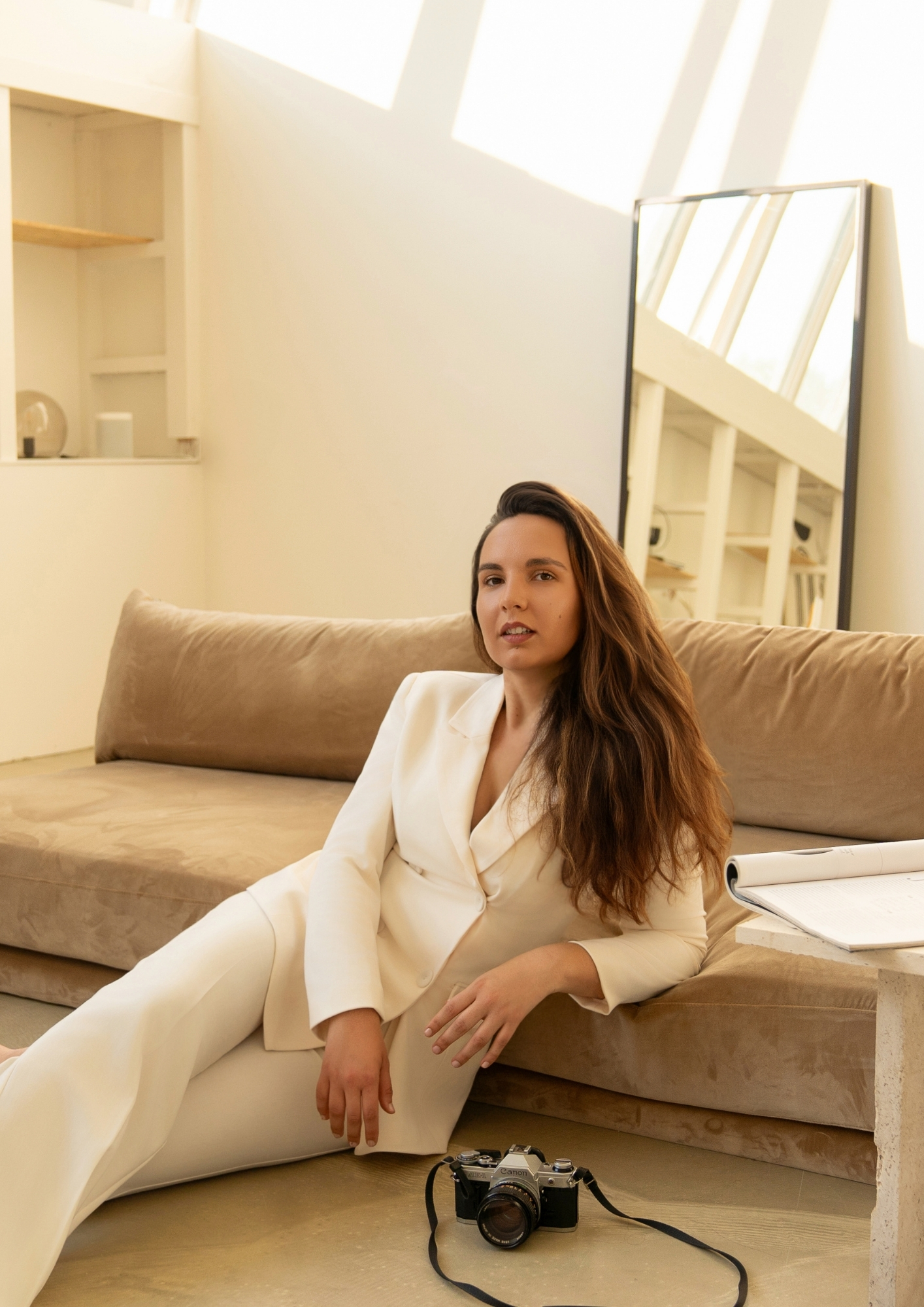Woman in a cream blazer sitting on a beige sofa in a bright, minimalist room
